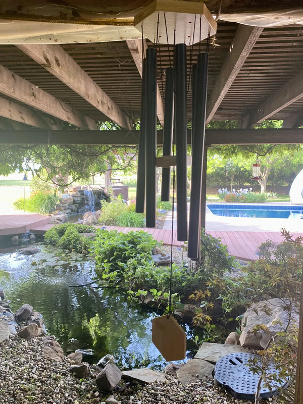 Black Wailua wind chime hanging under a deck above a garden pond, customer photo
