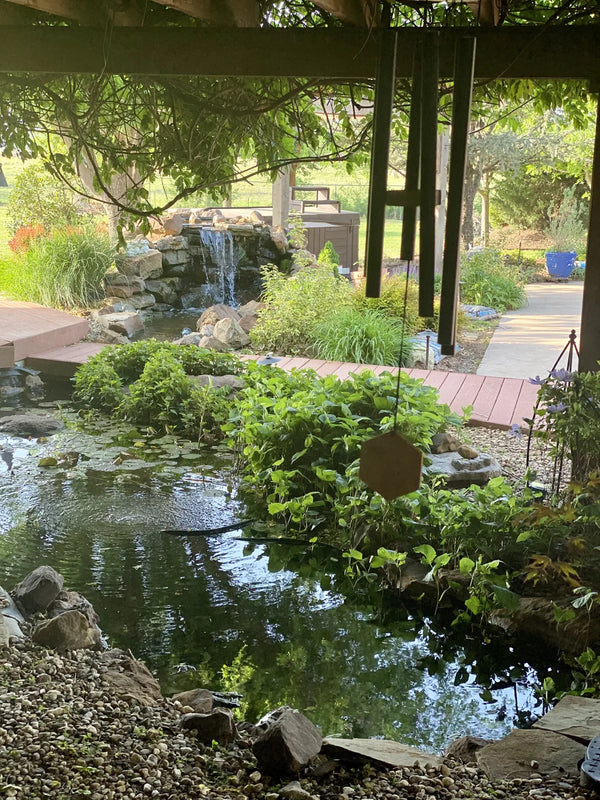 Black Wailua wind chime above a backyard pond and waterfall, customer photo