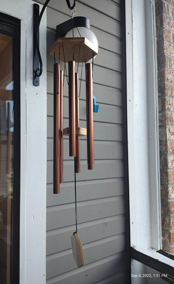Copper Wailua wind chime hanging on a wall bracket by a door, customer photo